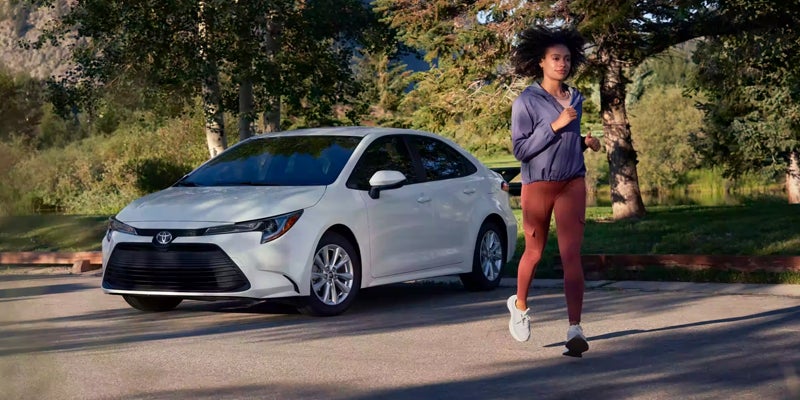 A jogger runs past a white corolla hybrid parked in the background.